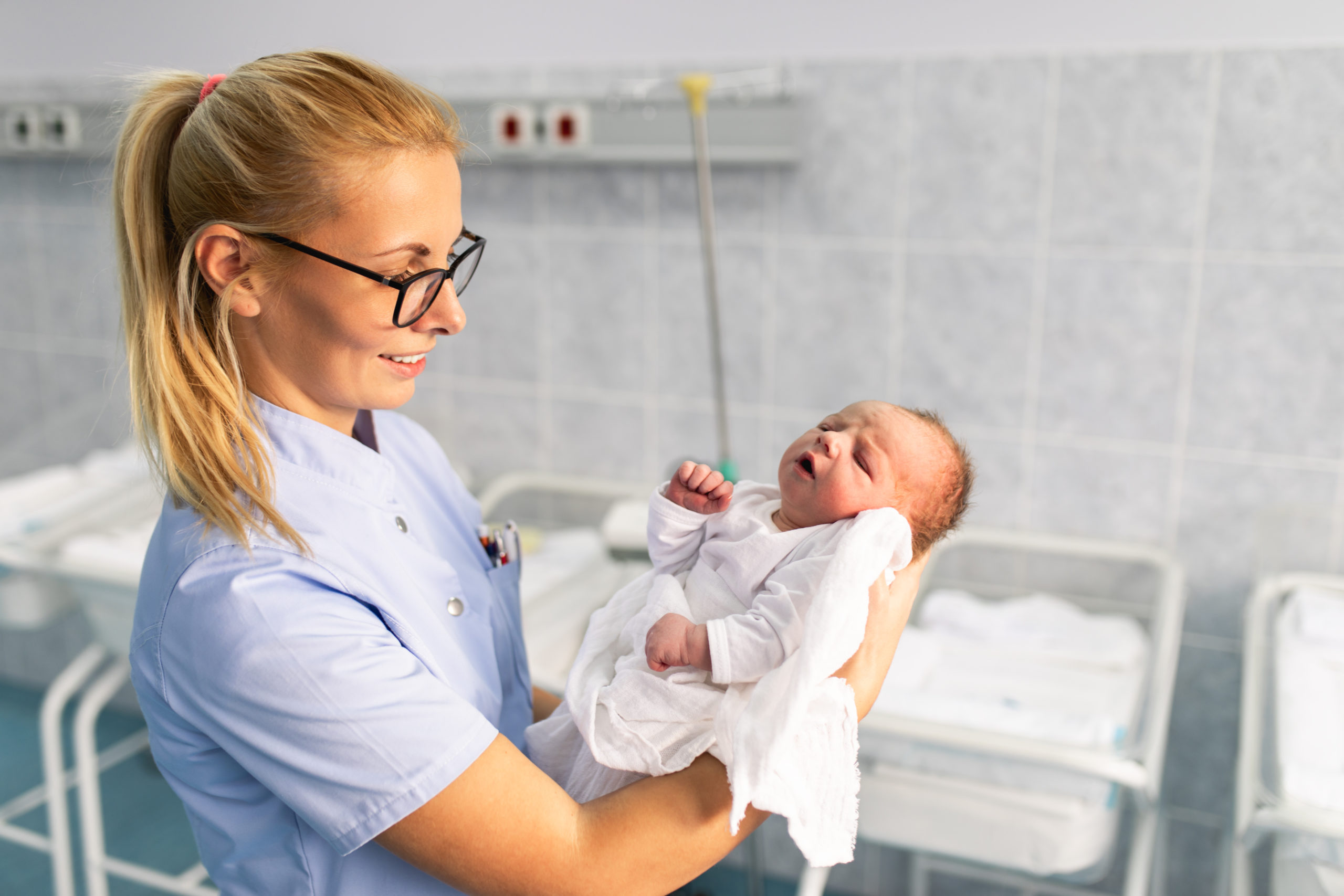Nurse midwife standing in maternity ward and holding newborn baby